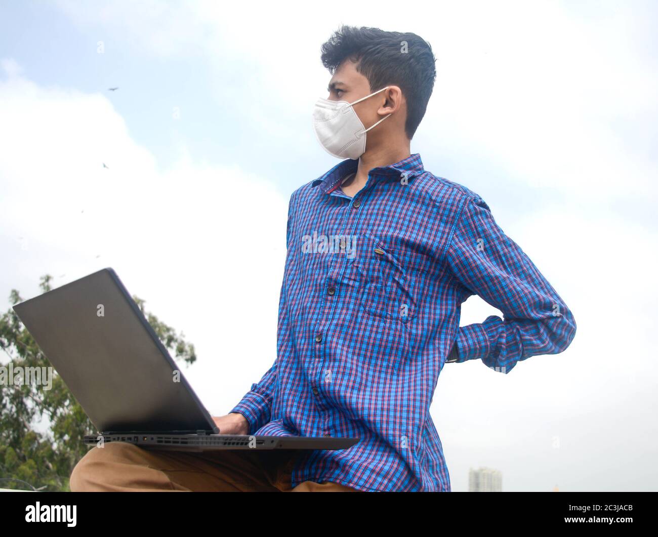 Adolescent homme travaillant dans ordinateur portable et regardant stressant avec douleur de dos . homme avec masque de protection du visage Banque D'Images