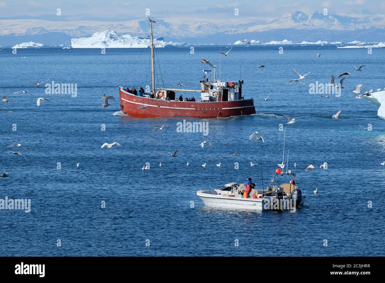 Les pêcheurs travaillent sur un petit bateau tandis qu'un chalutier de pêche navigue devant elle plus rentable 'capture' de touristes. Banque D'Images