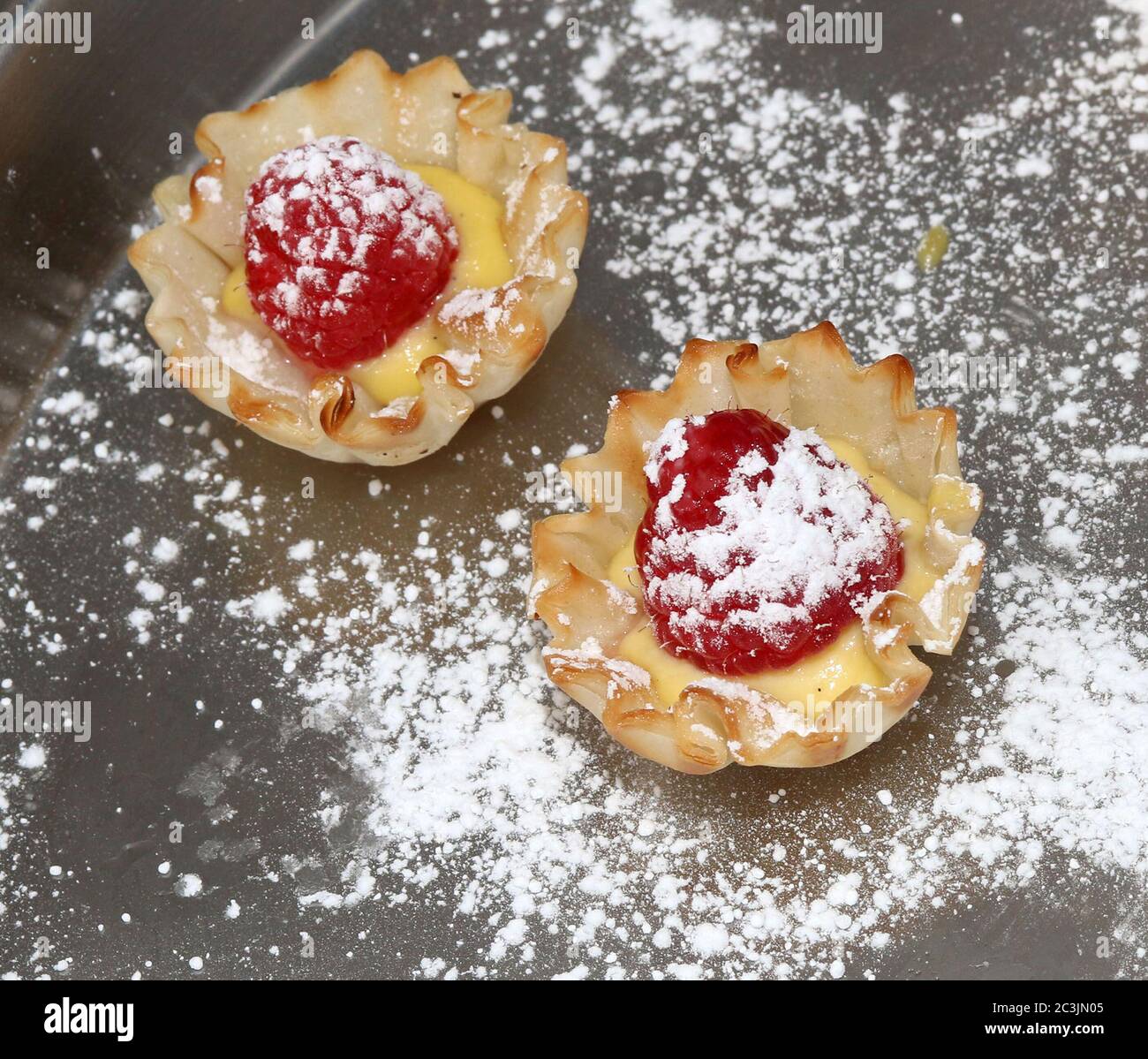Tarte aux framboises avec crème et sucre en poudre dans une tasse à pâtisserie Banque D'Images