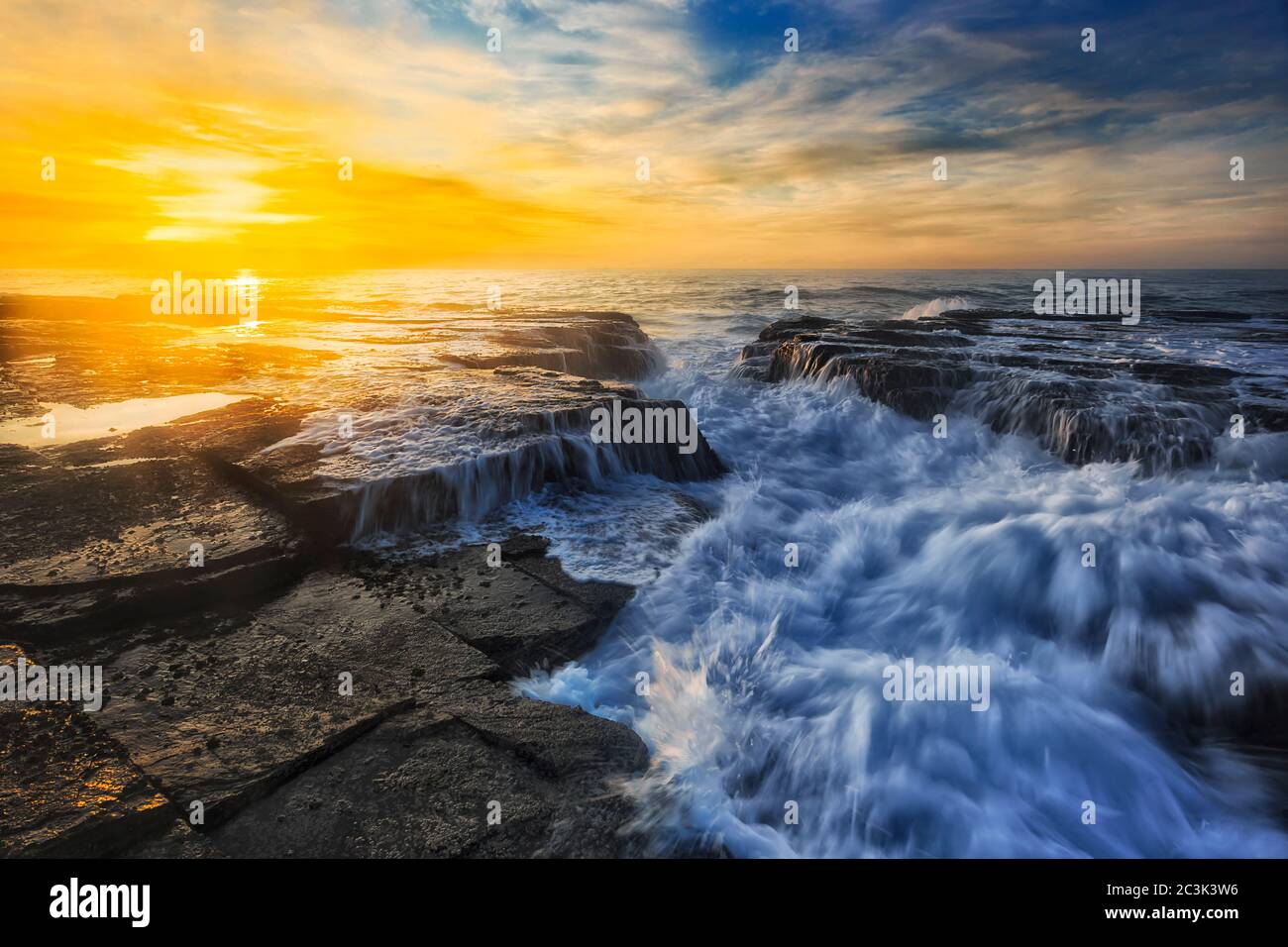 Vague rapide et forte qui frappe les rochers de grès dans une tranchée sur la plage de Narrabeen, sur la côte pacifique de Sydney, au lever du soleil. Banque D'Images