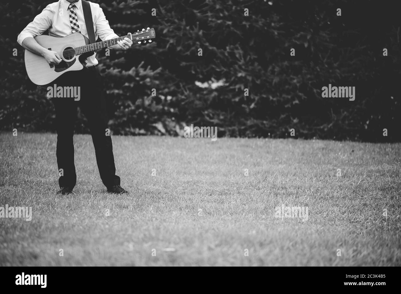 Prise de vue en niveaux de gris d'un homme solitaire jouant de la guitare un parc Banque D'Images