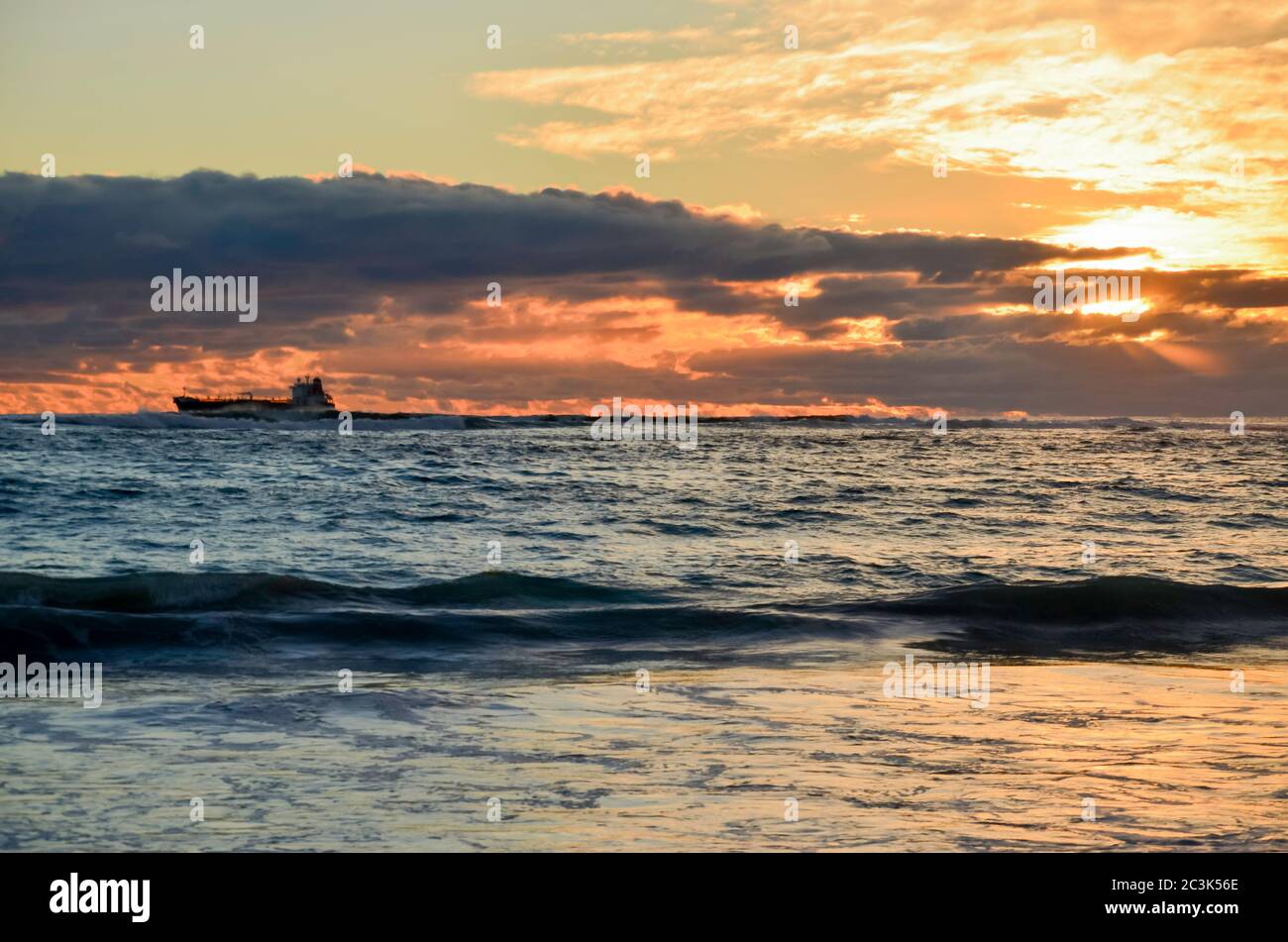 Un cargo côtier (cargo) silhouetté se déplace vers le sud sur la côte ouest de l'Australie au coucher du soleil Banque D'Images