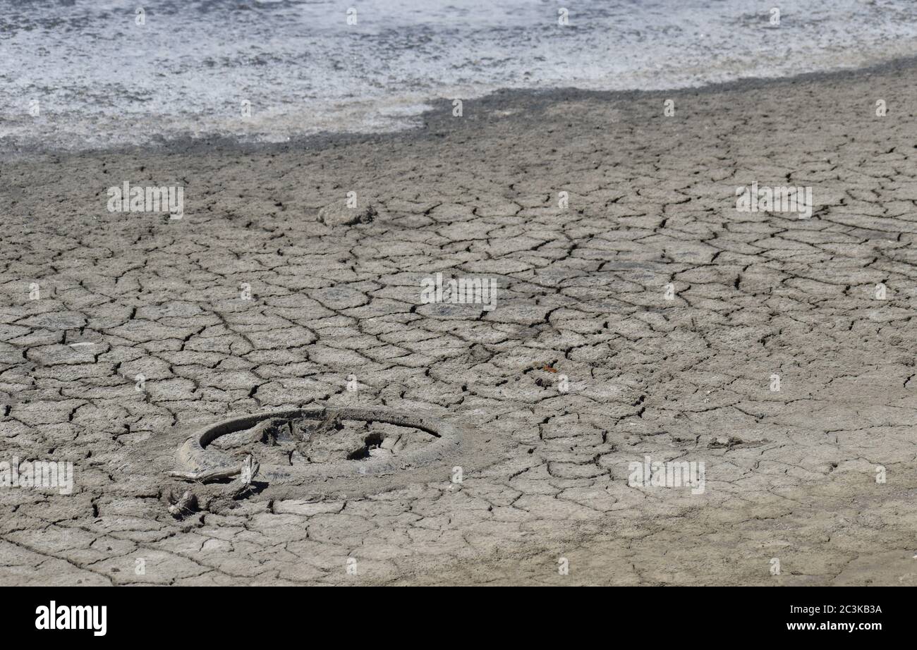 Un vieux pneu, enchâssés dans la boue craquée du lac en train de mourir, avec une croûte de sel au bord de l'eau Banque D'Images