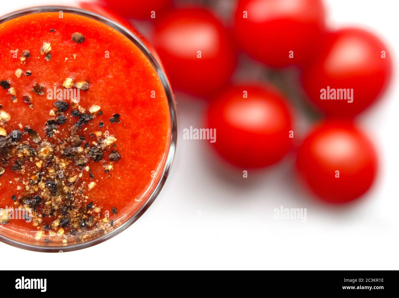 Coupe en verre avec jus de tomate, poivre noir moulu et tomates cerises sur fond blanc. Vue du dessus Banque D'Images