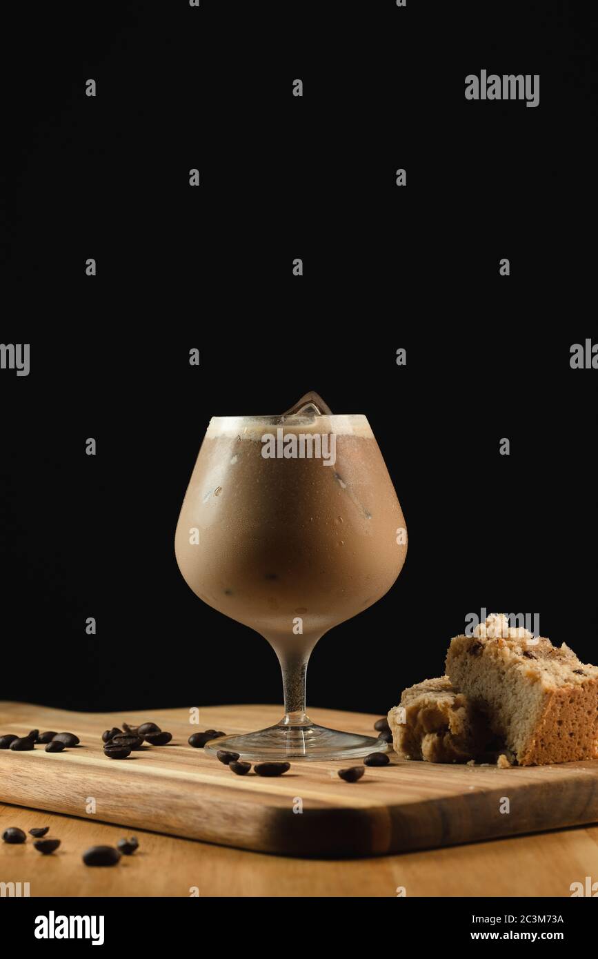 Gros plan d'un verre de cappuccino glacé sur un bois assiette avec décorations sur fond noir Banque D'Images