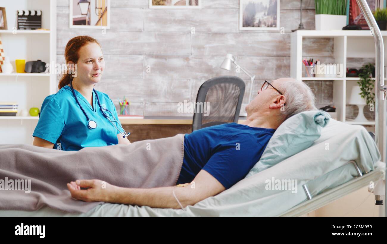 Homme âgé malade ayant une conversation avec une infirmière caucasienne alors qu'il était allongé dans un lit d'hôpital dans une maison de soins infirmiers Banque D'Images