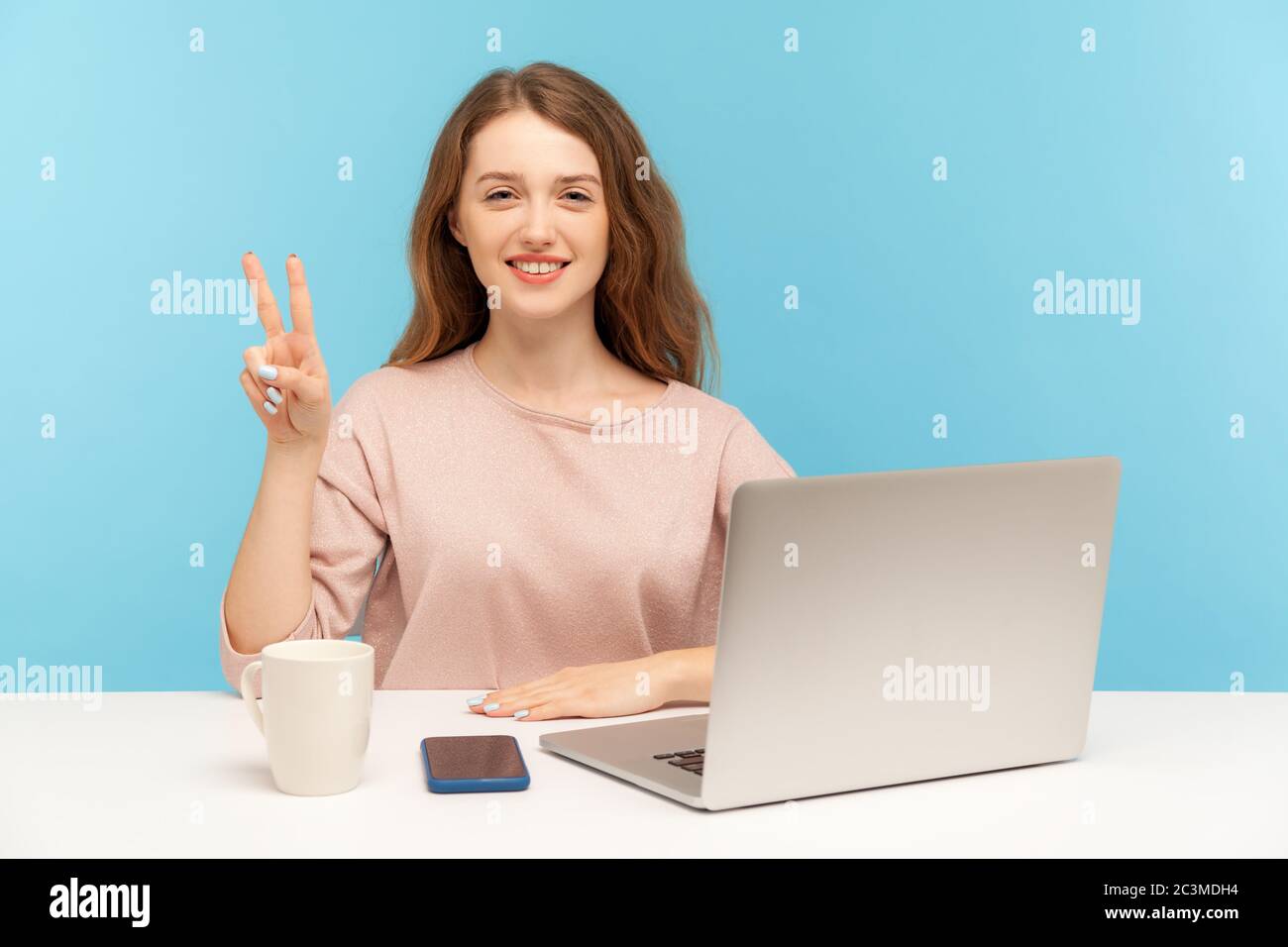 Jeune femme gaie, montrant le geste de la victoire, célébrant le projet réussi, faisant signe v avec les deux doigts au bureau à domicile de travail. ind Banque D'Images