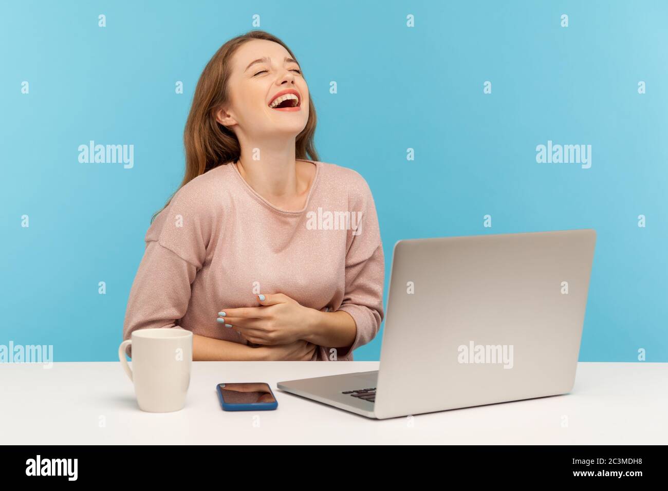Une femme heureuse et amusante, qui rit à voix haute, tient le ventre et se fait hystérie par une blague folle sur un ordinateur portable, se faisant une pause au bureau à domicile Banque D'Images