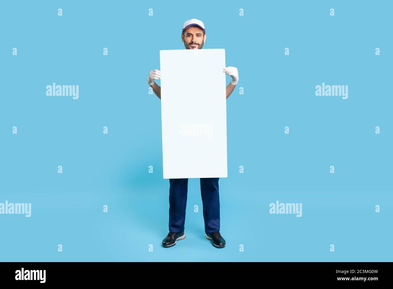 Portrait de l'homme en casquette et gants de protection tenant un modèle d'affiche de feuille vide vertical, maquette espace vide pour le message publicitaire, réf Banque D'Images