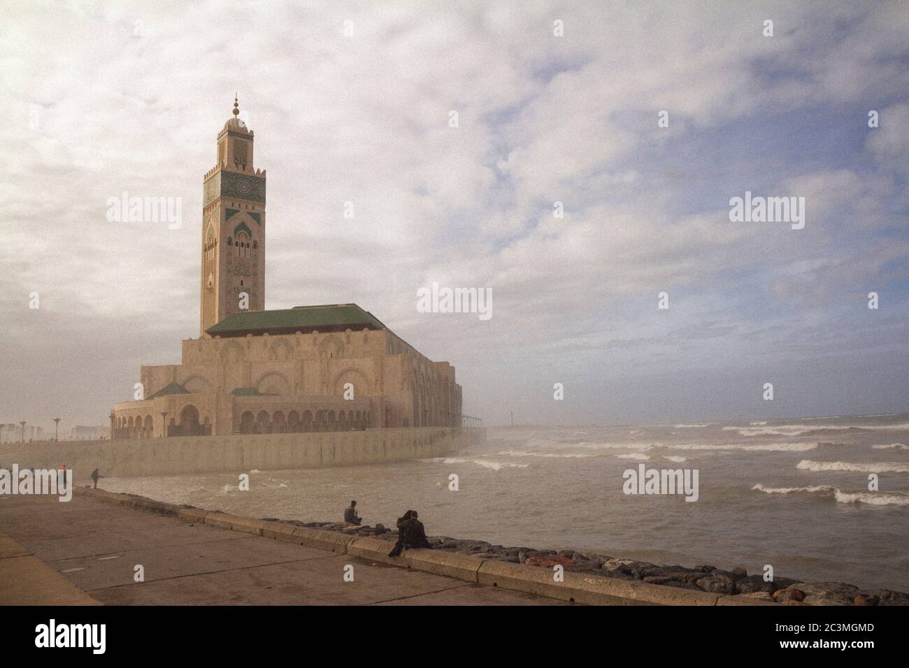 Un groupe de personnes marchant et assis autour de la mosquée Hassan II à Casablanca, au Maroc, pendant un après-midi brumeux, profitant de la vue sur l'océan Banque D'Images