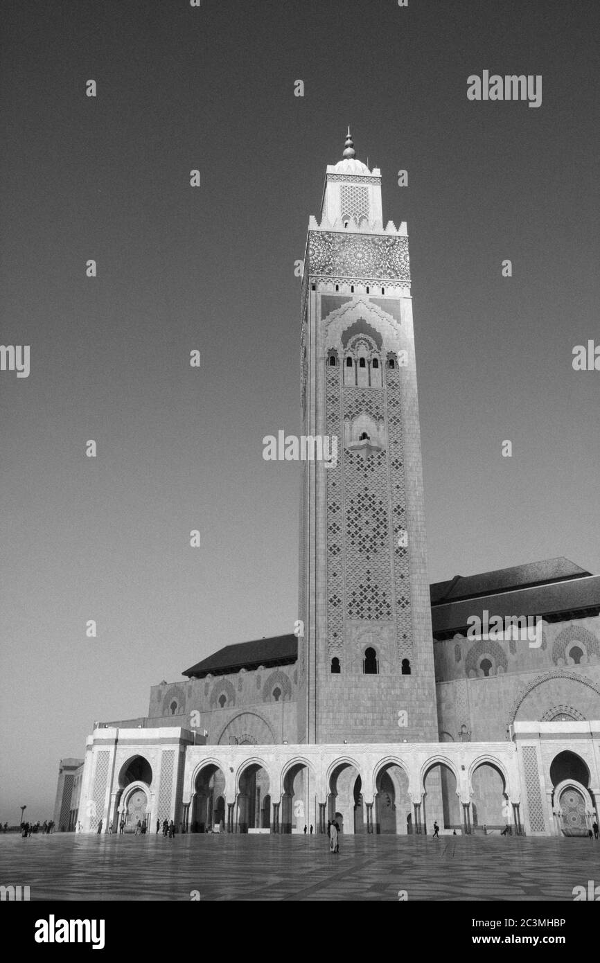 Un groupe de personnes marchant et assis autour de la mosquée Hassan II à Casablanca, au Maroc, pendant un après-midi brumeux, profitant de la vue sur l'océan Banque D'Images