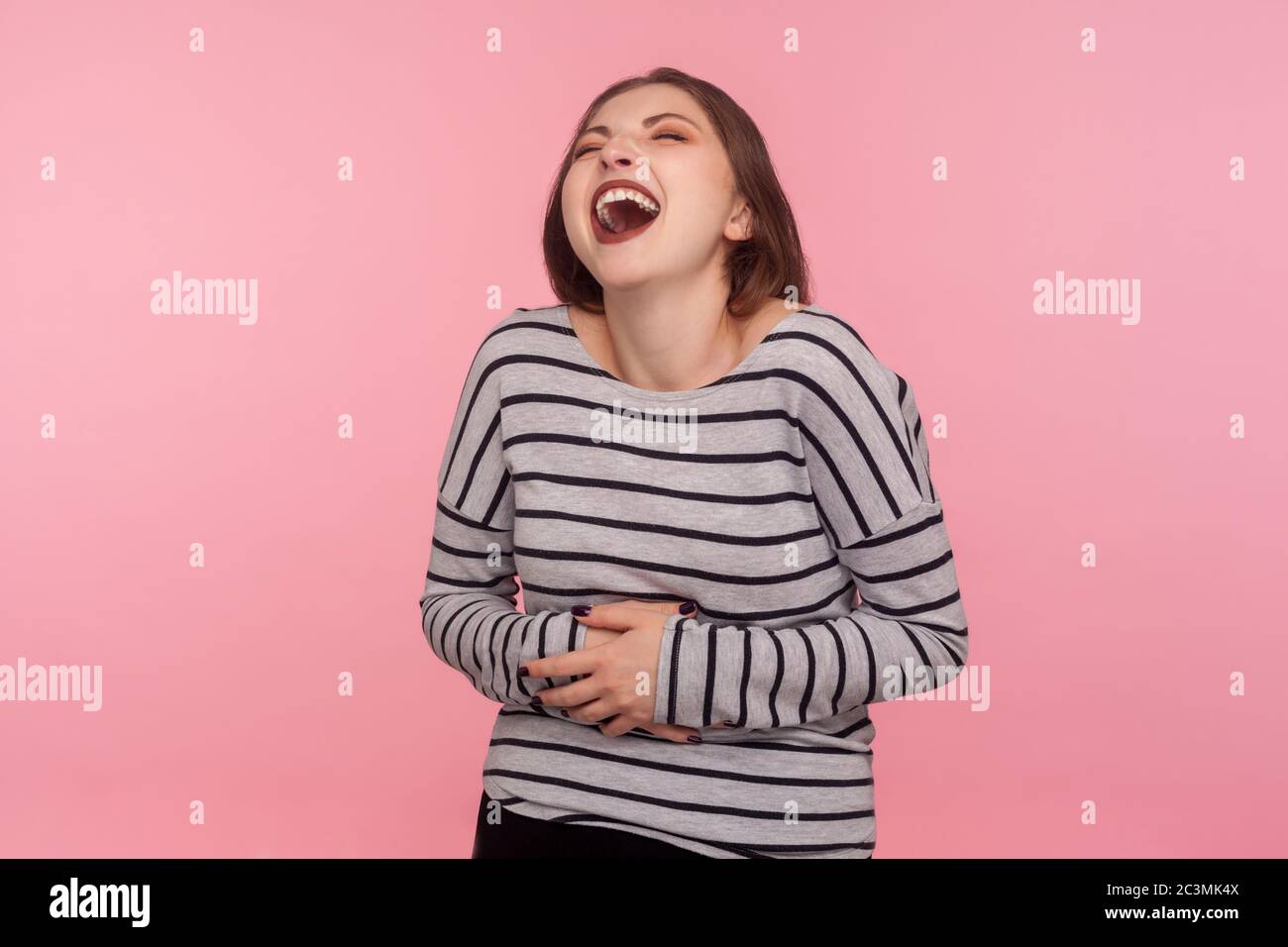 Portrait de femme amusée dans un sweat-shirt rayé tenant l'estomac, ne peut pas arrêter de rire fort, craquer et être hystérique à la plaisanterie drôle, anecdote. Dans Banque D'Images