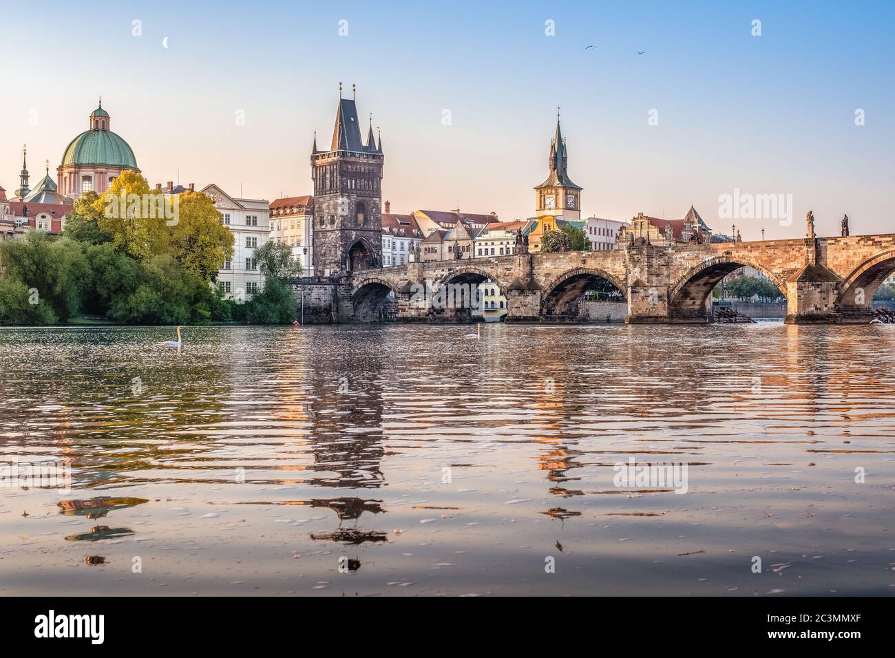 Pont Charles sur la Vltava avec cygnes au lever du soleil tôt le matin avec encore la lune visible sur le ciel, Prague, République Tchèque --- NIKON D750 Banque D'Images