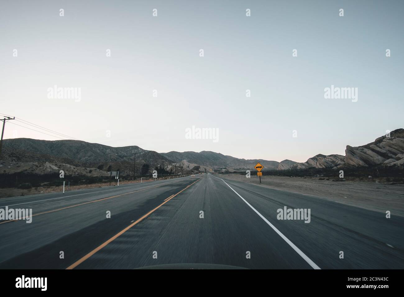 Autoroute vide en Californie juste après le coucher du soleil avec le panneau de route jaune et les montagnes dans la distance pendant la pandémie de coronavirus Banque D'Images