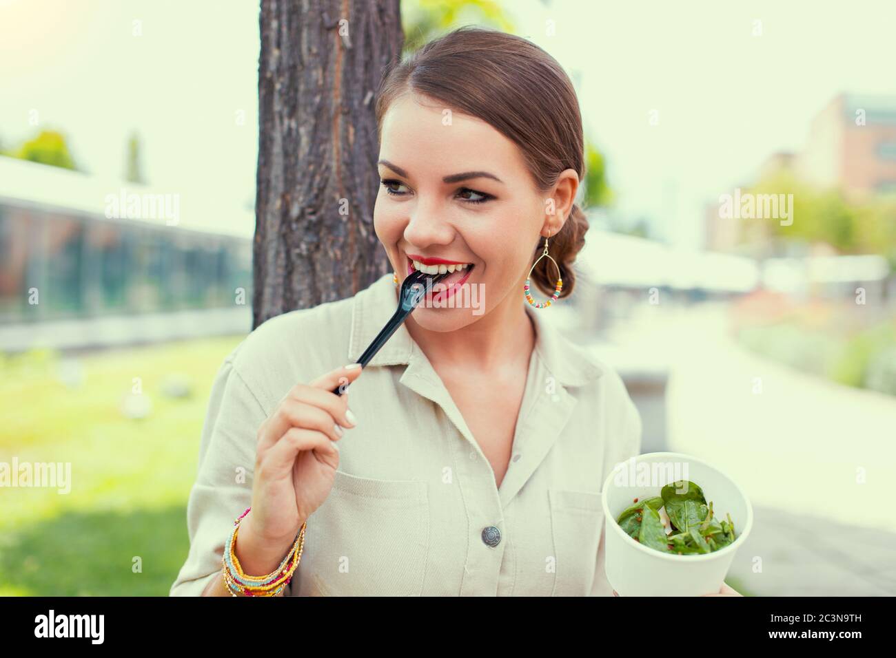 Jeune femme de latina joyeuse appréciant manger de la salade dans le parc, en regardant loin Banque D'Images