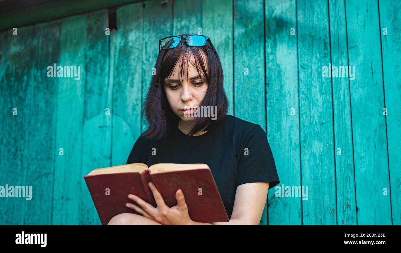 Gros plan de la jeune femme lisant le livre sur fond de la vieille maison en bois. Banque D'Images