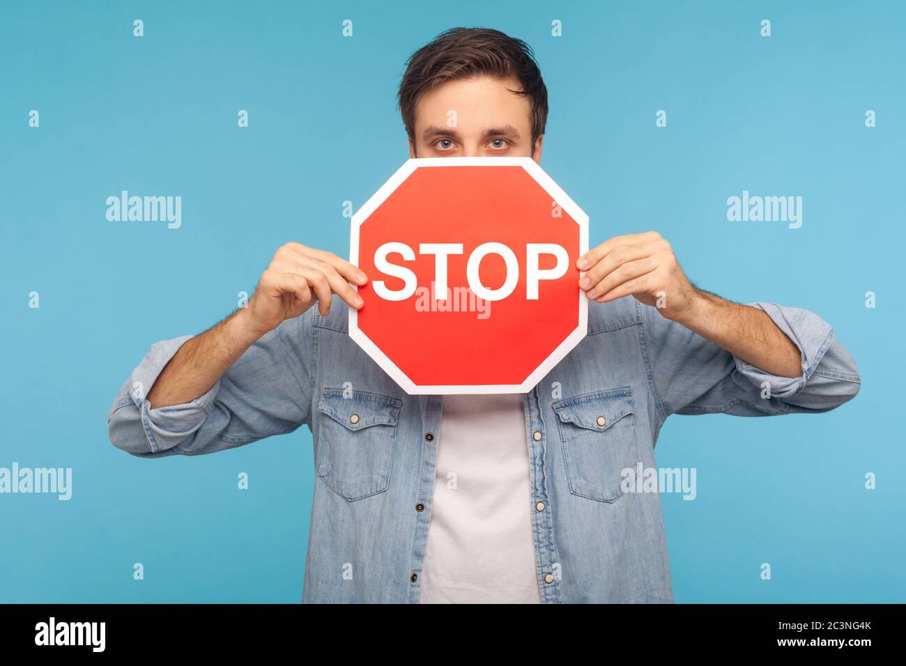 Méthode interdite! Portrait d'un homme dans une chemise en denim ouvrier qui se trouve à l'extérieur du panneau de signalisation routière Stop, montrant le symbole des restrictions et de l'accès interdit. indo Banque D'Images