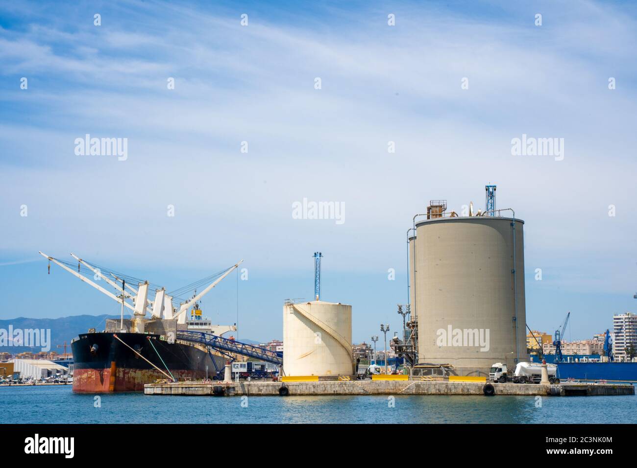 Grands conteneurs industriels dans le port à côté d'un navire avec grues et camions Banque D'Images