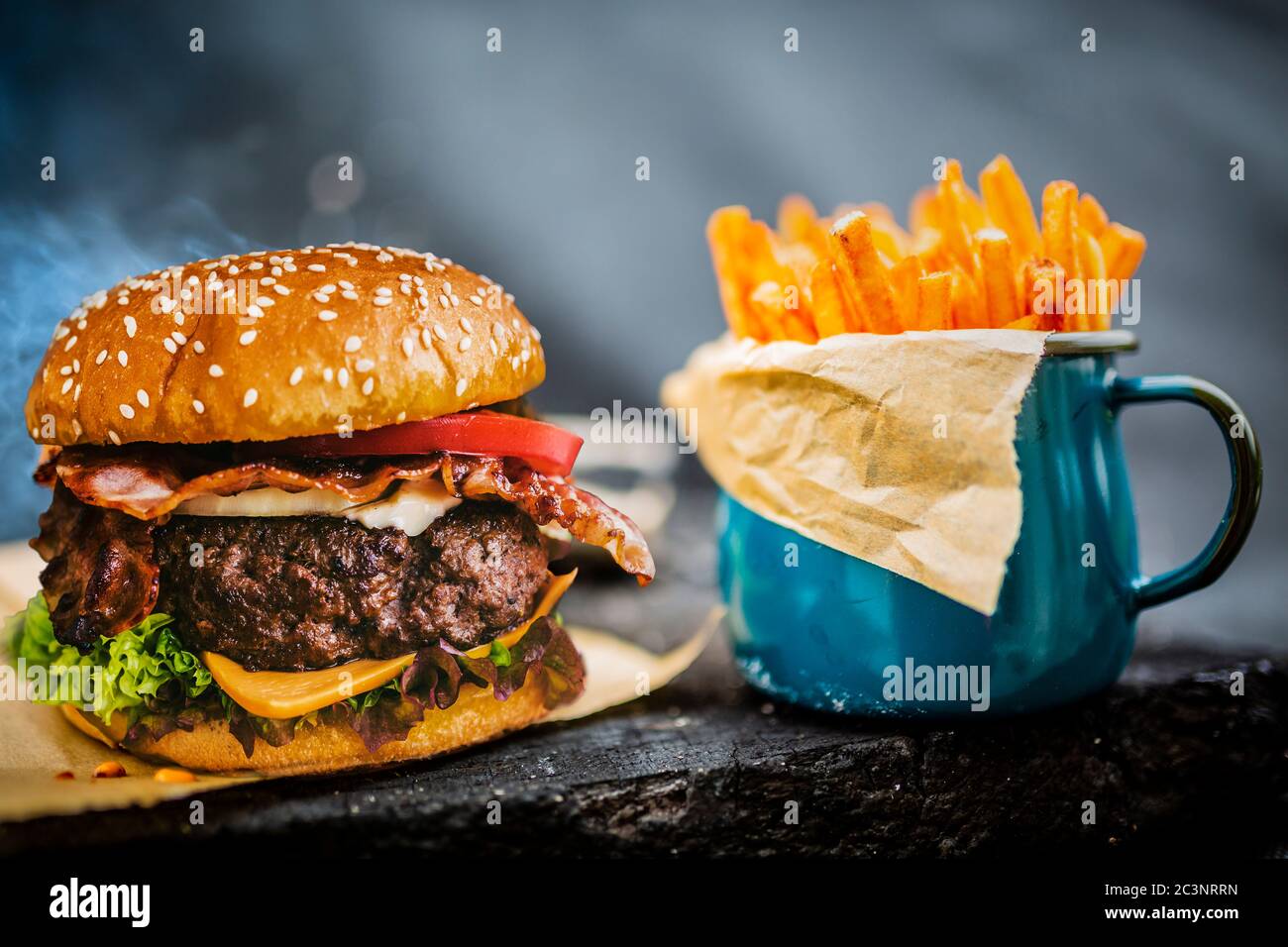 Savoureux hamburger de bœuf grillé avec laitue aux épinards et fromage bleu servi avec des frites sur une table en bois avec espace d'imitation, tableau noir en arrière-plan. Banque D'Images
