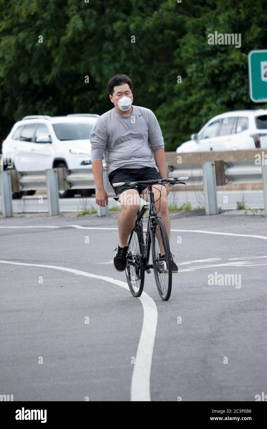 Un homme américain asiatique, probablement coréen, se met en vélo sur un sentier près de Cross Island Parkway, portant un masque et un casque. À Bayside, Queens, New York. Banque D'Images