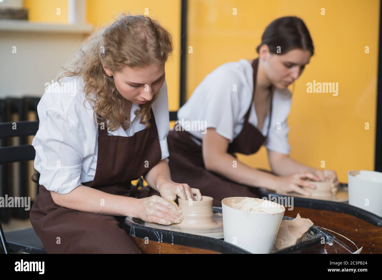 Deux artistes de céramique femelle en tablier utilisant du matériel d'argile travaillant dans le studio de potter. Formation à distance en soirée. Aventure de loisirs pour adultes. Hiver Banque D'Images