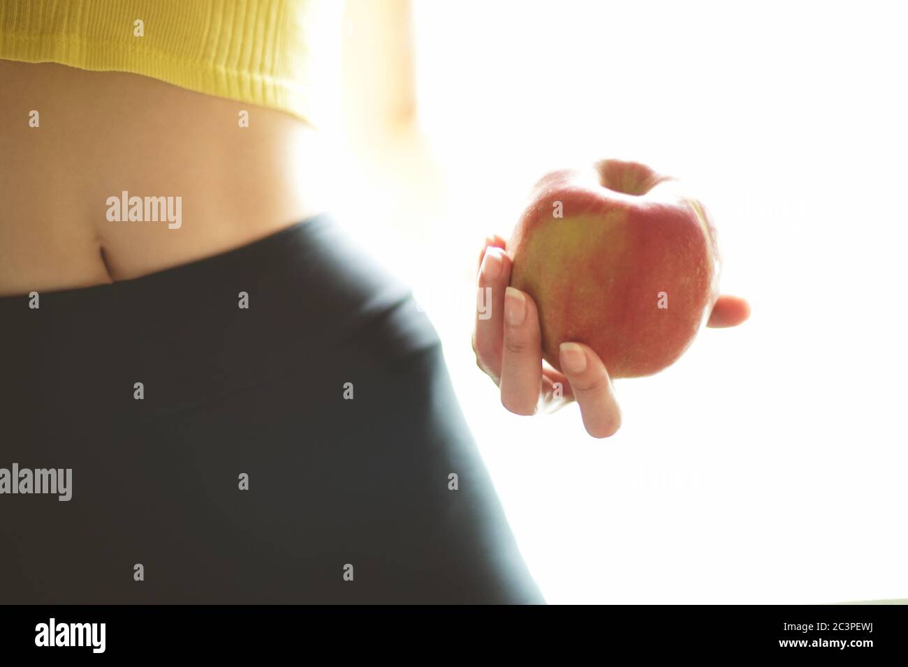 Pomme rouge dans une main femelle. Jeune corps athlétique d'une fille avec leggings et haut. Forme physique et santé Banque D'Images