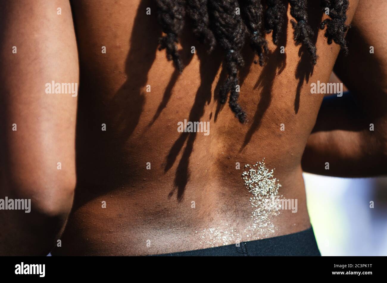 Gros plan d'un dos sablonneux avec des dreadlocks jetant des ombres sur la peau brune sur le dos d'un homme américain à la plage de Miami, Floride, États-Unis Banque D'Images