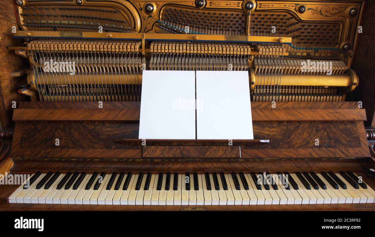 Vue avant d'un piano en bois antique avec clavier ouvert et deux feuilles de papier blanc sur le support des notes musicales Banque D'Images