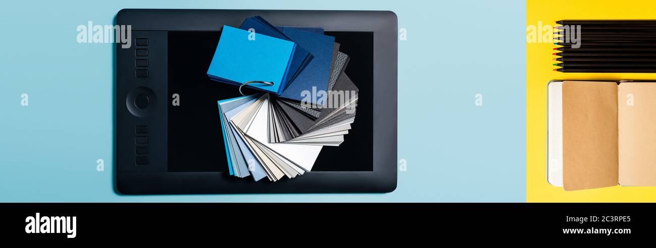 Collage d'échantillons de couleur sur une tablette graphique et un bloc-notes avec crayons sur fond bleu et jaune Banque D'Images