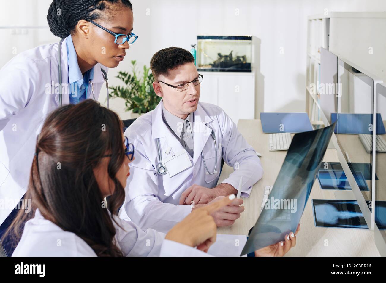 Groupe de jeunes médecins concernés discutant de la radiographie pulmonaire d'un patient soupçonné de COVID-19 Banque D'Images