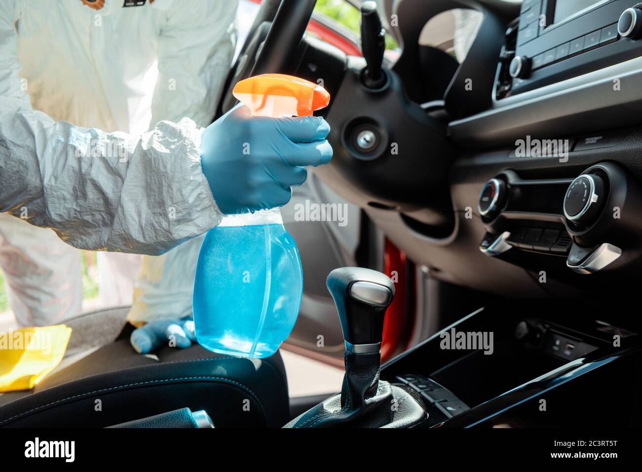 vue de culture d'un spécialiste en costume de noisette nettoyant l'intérieur de la voiture avec un spray antiseptique pendant une pandémie de coronavirus Banque D'Images
