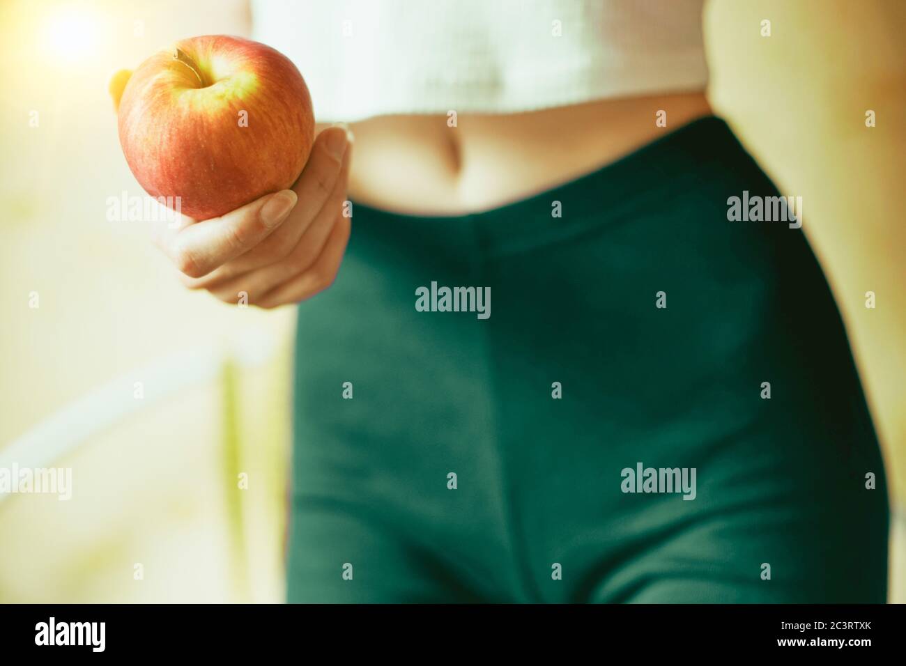 Pomme rouge dans une main femelle. Jeune corps athlétique d'une fille avec leggings et haut. Concept de forme physique et de santé Banque D'Images