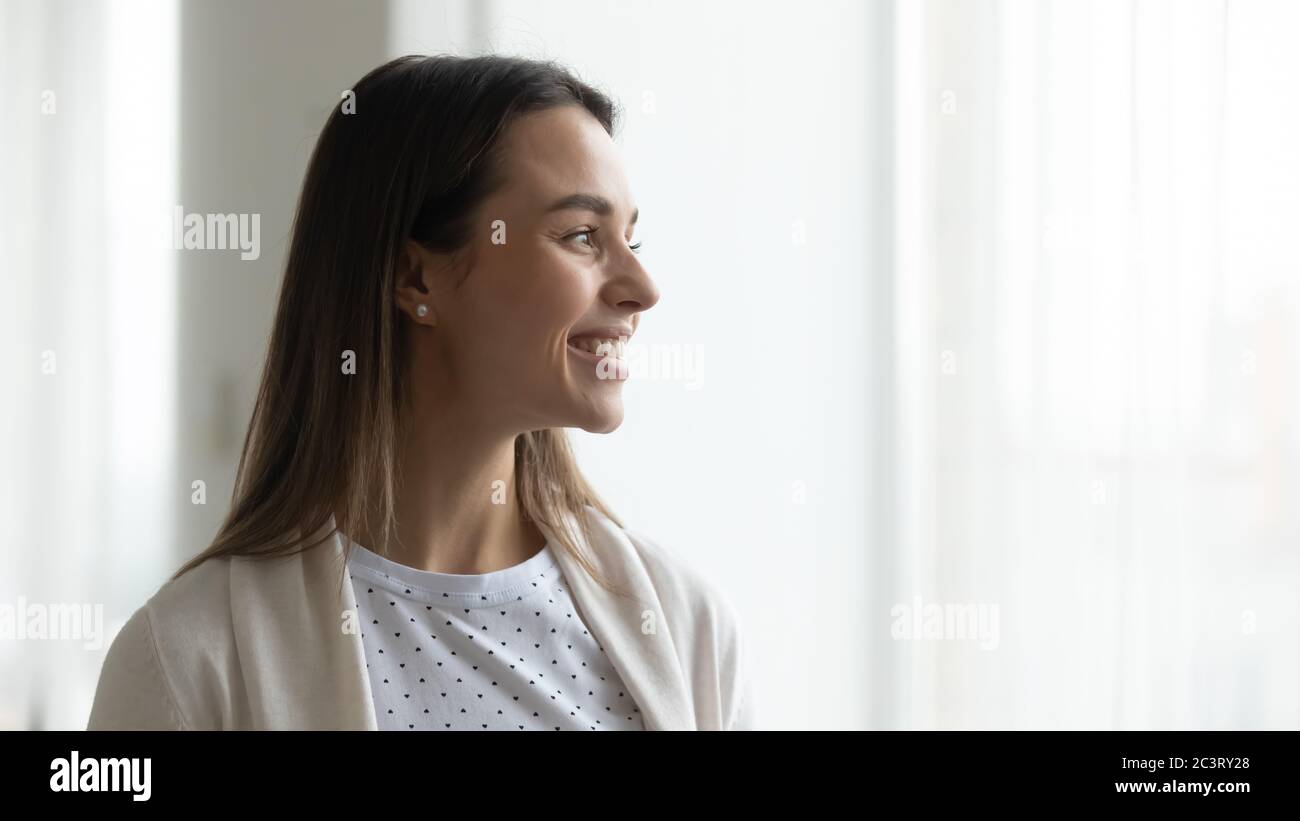 Une jeune femme heureuse se tenant près de la fenêtre, en regardant loin sourire Banque D'Images