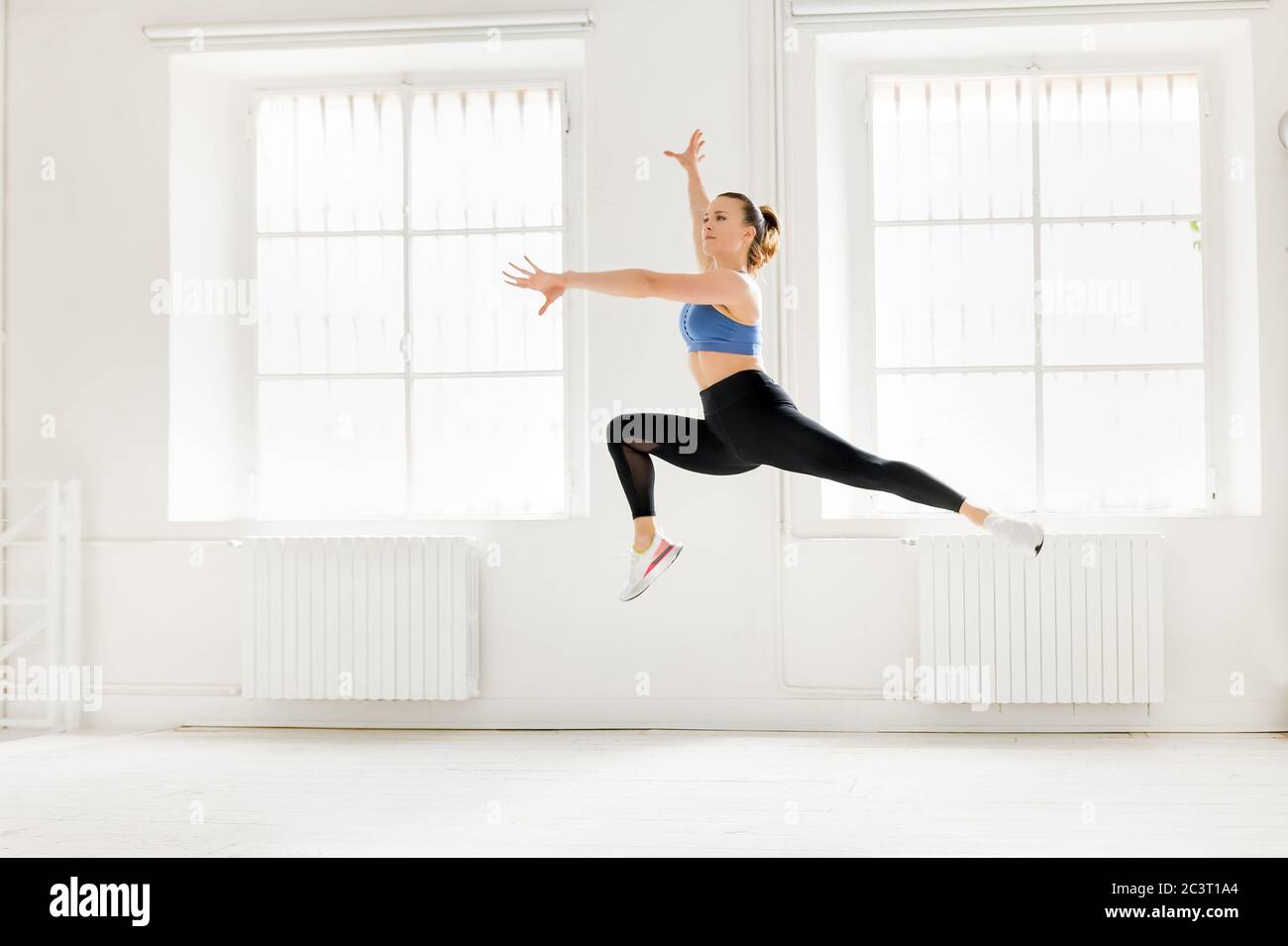 Femme exécutant un saut gymnastique enjambé en bondissant gracieusement dans l'air avec les bras étirés dans une salle de gym haute clé dans un conce de santé et de forme physique Banque D'Images