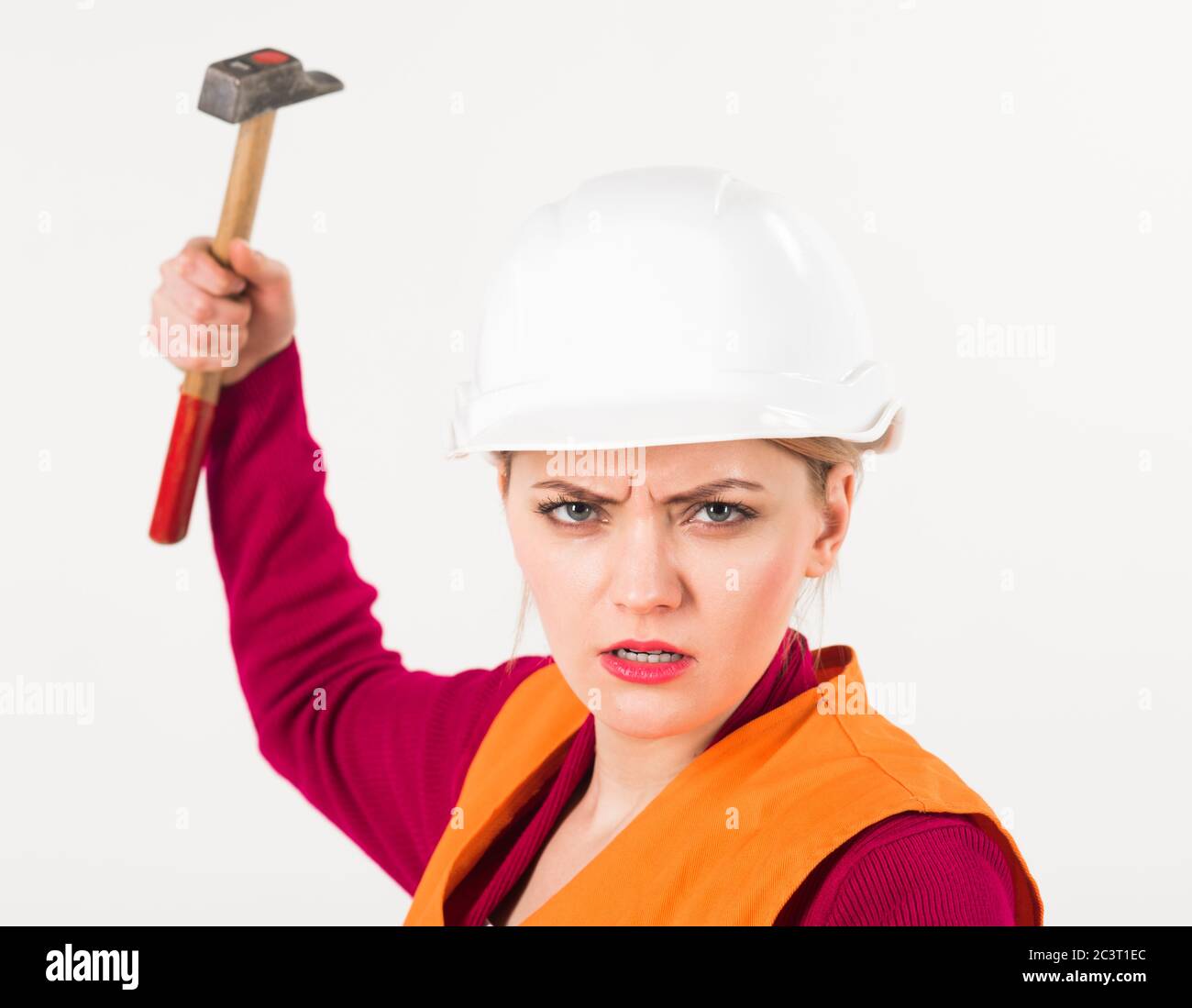 Concept fort et indépendant. Femme avec le visage sérieux tient le marteau, isolé sur fond blanc. La jeune femme travaille comme constructeur. Fille dans un casque ou un casque de sécurité va s'écraser avec un marteau. Banque D'Images