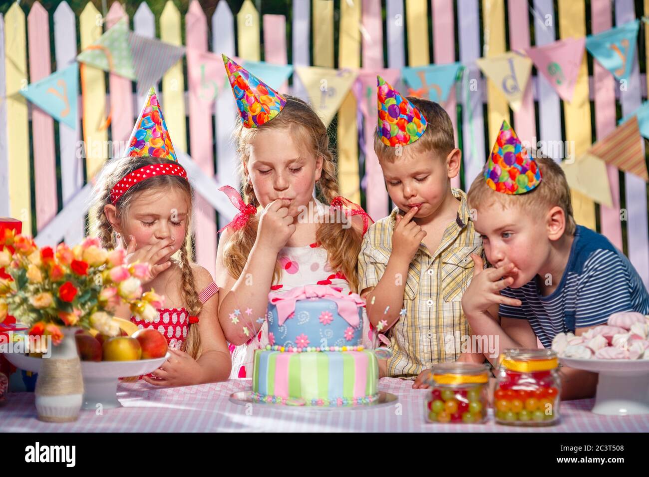 Les petits enfants se réjouissent à l'anniversaire de la fille, en testant le gâteau et la crème à lécher sur les doigts Banque D'Images