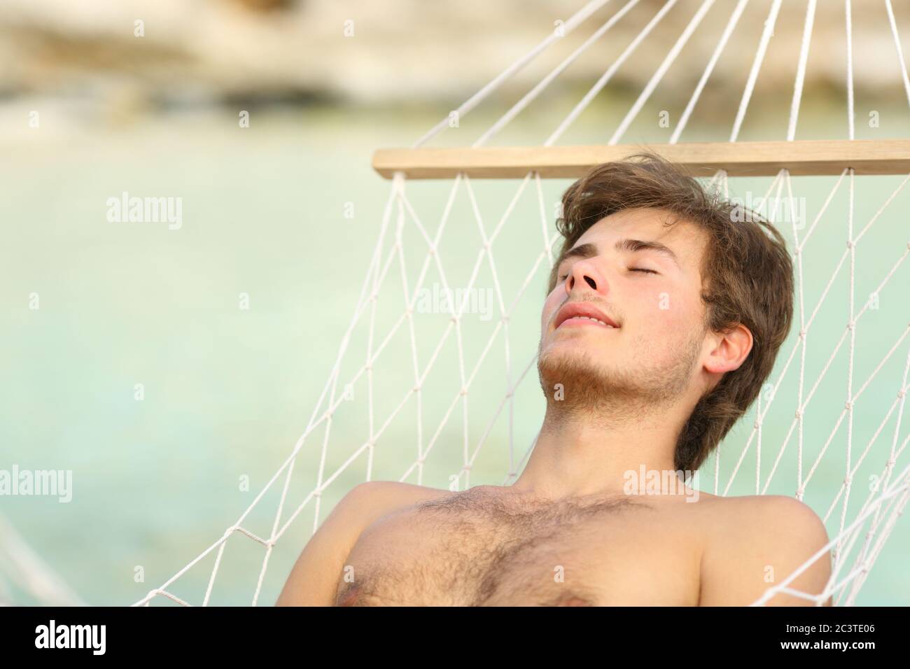 Homme sans chirte décontracté, bain de soleil, reposant sur un hamac au bord de la plage Banque D'Images
