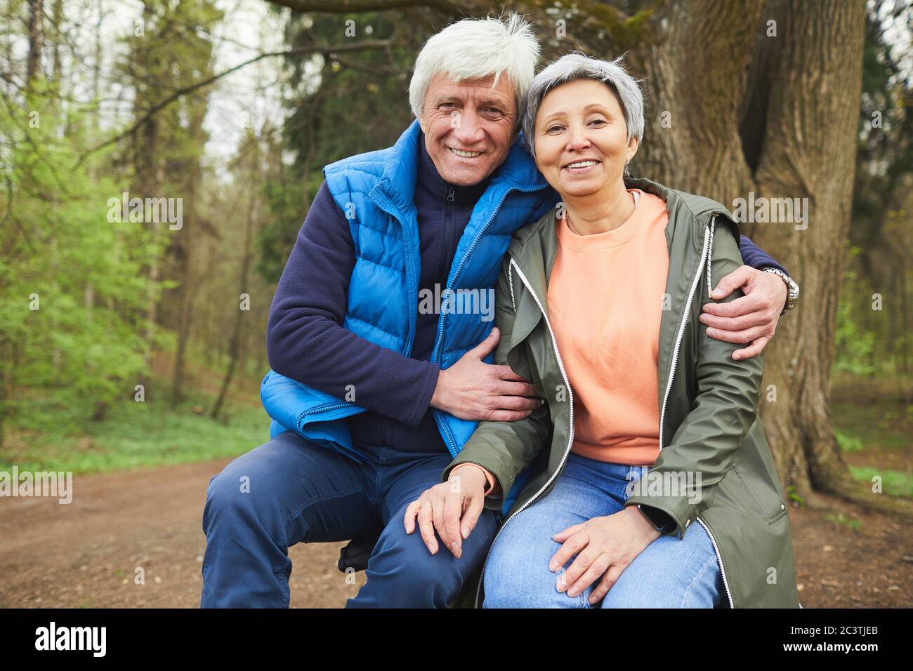 Portrait d'un couple senior actif souriant regardant avec joie l'appareil photo tout en posant pendant la randonnée dans la forêt d'automne, espace de copie Banque D'Images