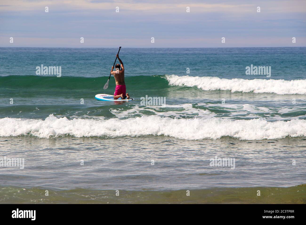 Semelle debout paddle boarder s'agenouiller tout en pagayant contre les vagues pour aller en mer Banque D'Images