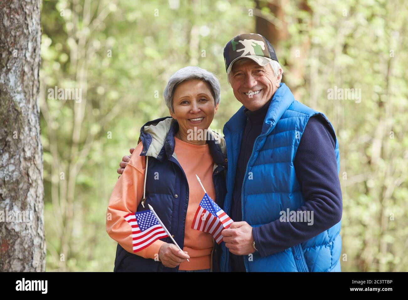Portrait à la taille du couple senior actif tenant des drapeaux américains et regardant l'appareil photo tout en appréciant la randonnée dans la forêt, espace de copie Banque D'Images