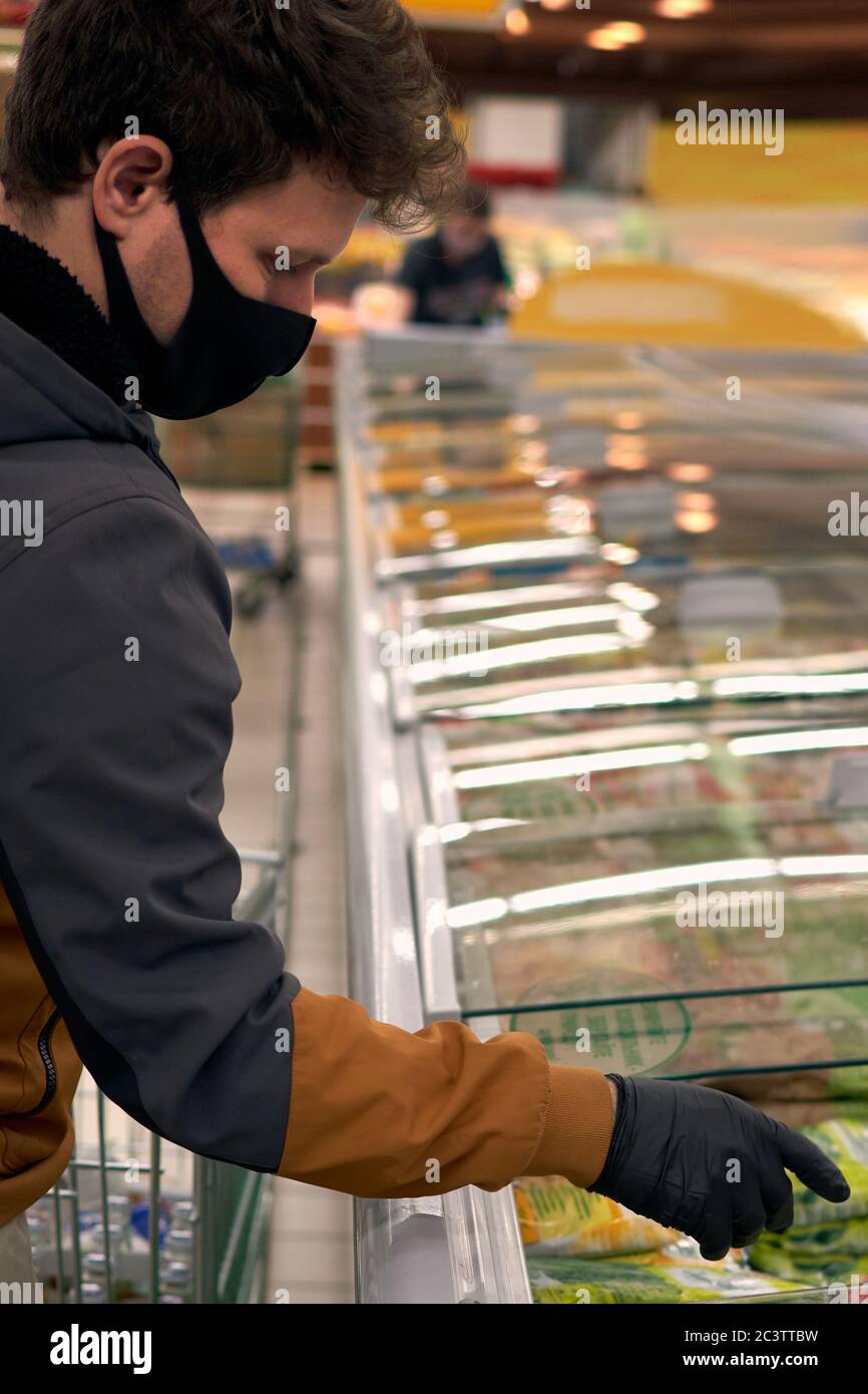 Homme dans le masque médical jetable et gants d'achat dans le supermarché. Panique shopping pendant la pandémie de covid-19 du coronavirus. Banque D'Images