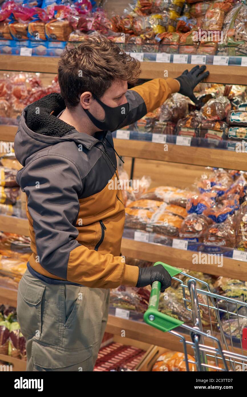 Homme dans le masque médical jetable et gants d'achat dans le supermarché. Panique shopping pendant la pandémie de covid-19 du coronavirus. Banque D'Images