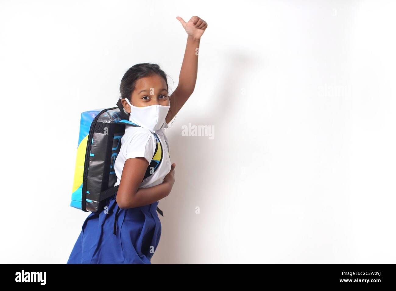 Enfant fille avec l'uniforme et le masque d'école excitée de retourner à l'école après Covid-19 verrouillage. Isolé sur fond blanc. Banque D'Images