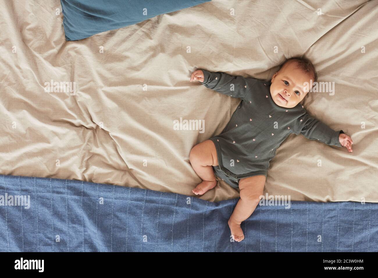 Vue de dessus de bébé de course mixte mignon couché sur un lit confortable avec des couvertures bleues et blanches moelleuses, espace de copie Banque D'Images