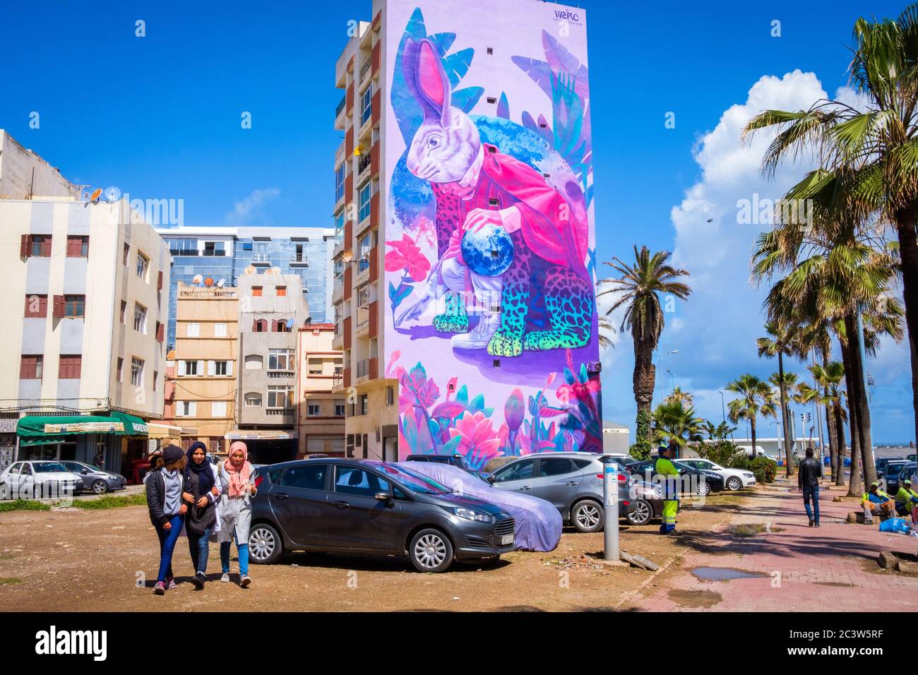 Maroc, Casablanca: Bâtiments et murale dans le boulevard Zerktouni. Trois filles marchant devant des bâtiments et une murale représentant un lapin géant, oeuvre de Mexica Banque D'Images