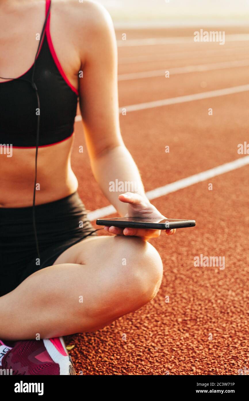 Athlète féminine détendue assise sur la piste de course après l'entraînement Banque D'Images