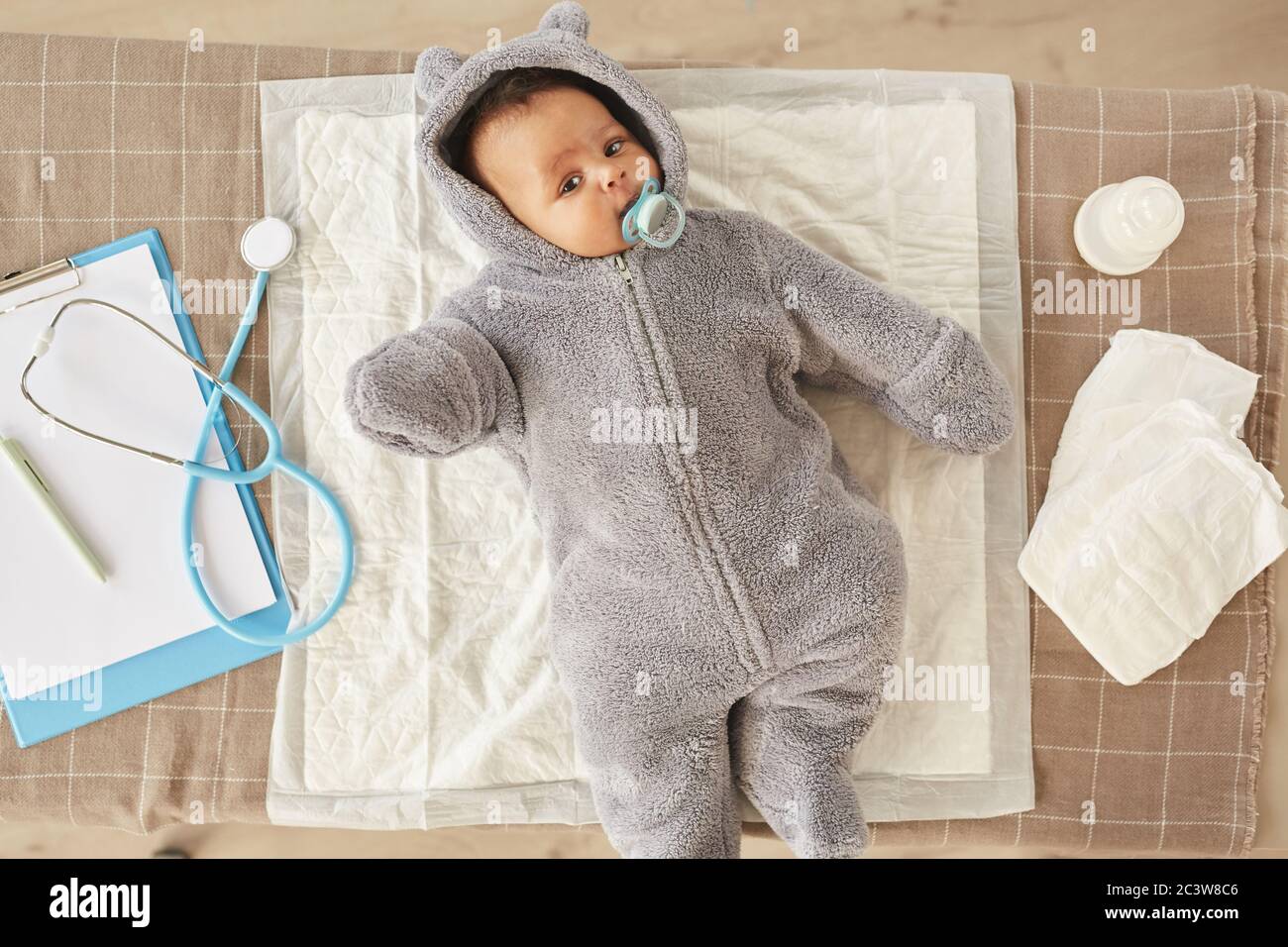 Au-dessus de la vue sur un adorable bébé afro-américain portant une combinaison en peluche, allongé sur une table à langer pendant le contrôle au bureau du médecin, espace copie Banque D'Images