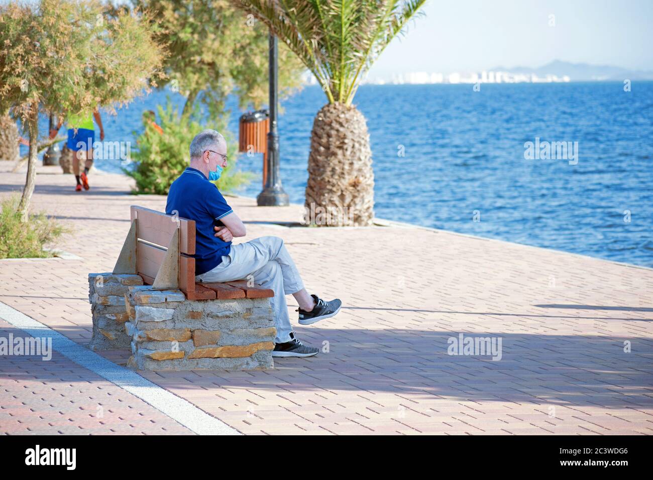 Homme senior assis sur un banc en bois observant Lo Pagan paysage marin à Murcie Espagne, après le verrouillage du coronavirus. Banque D'Images