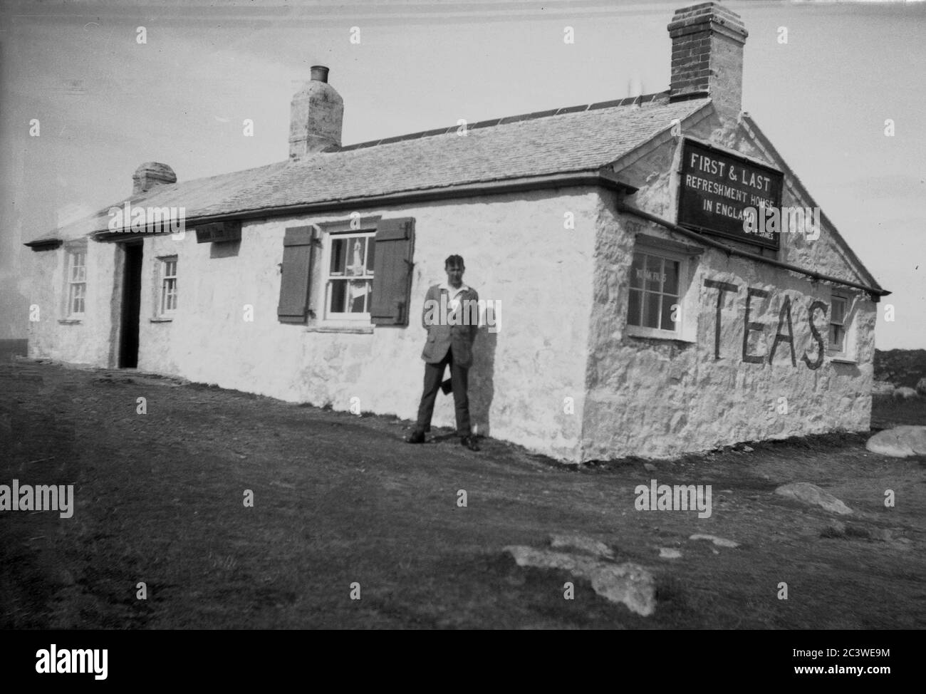 Vers les années 1940, historique, homme debout devant un cottage en pierre blanchie à la chaux d'un seul étage avec un panneau sur le mur lointain disant, 'First & Last' Refreshment House en Angleterre. Ce célèbre cottage situé sur les plateaux de la côte à l'extrémité de Land à Cornwall, dans l'extrême sud-ouest de l'Angleterre, est également connu comme la « première et dernière maison en Angleterre et a été inauguré par une dame appelée Gracie Thomas, qui a servi des repas, des boissons et des souvenirs aux voyageurs. Banque D'Images