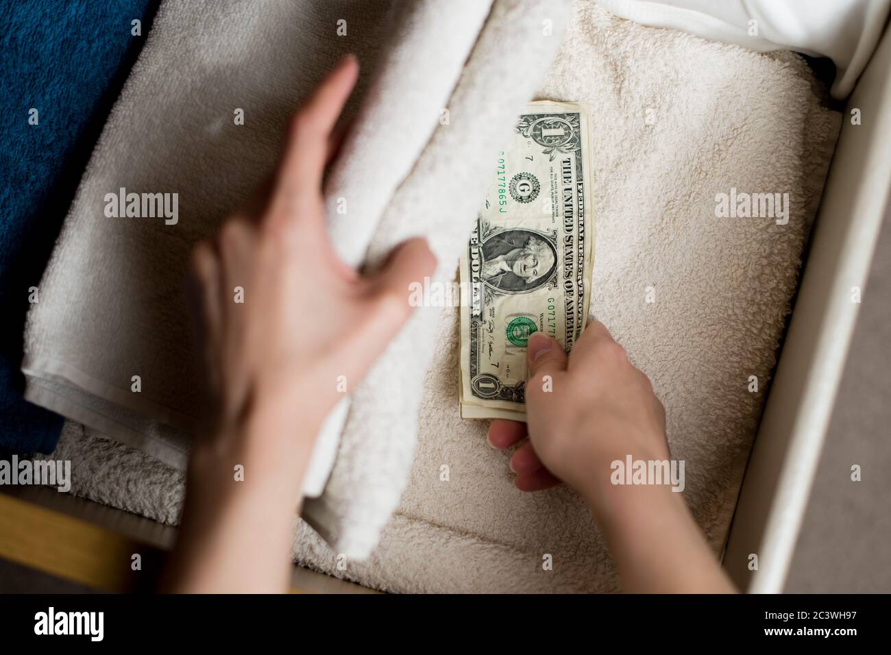 une main prend ou met une petite pile de froissés billets de dollars dans une boîte à serviettes Banque D'Images